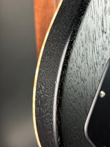 Close-up detail of a black electric guitar body showing the glossy wood grain finish, edge contour, and a sliver of the light-colored binding.