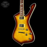 A classic electric guitar with a sunburst finish, featuring a dark brown outer edge fading to a bright yellow-orange center. It has gold hardware, including pickups, bridge, and tuners, and is set against a solid black background with a Tone Shop watermark in the top-left corner.