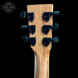 Close-up of the headstock of a guitar with a natural wood grain finish and six black tuning pegs, shown against a solid black background. A Tone Shop watermark is visible in the top left corner.