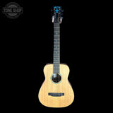 A natural wood acoustic guitar with a black headstock and black neck, shown vertically against a solid black background. A circular 'TONE SHOP' watermark is visible in the top-left corner.