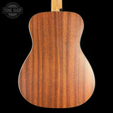 Close-up of the back of an acoustic guitar showing a rich, warm brown wood grain finish, set against a solid black background with a Tone Shop logo in the top-left corner.