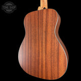 Close-up of the back of an acoustic guitar showing a rich, warm brown wood grain finish, set against a solid black background with a Tone Shop watermark in the top left corner.