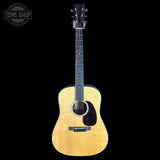 A natural wood acoustic guitar with a dark headstock, shown vertically against a solid black background. A circular 'TONE SHOP' watermark is visible in the top-left corner.