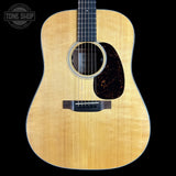 A natural wood acoustic guitar shown from the front against a solid black background, featuring a flamed maple top, dark pickguard, and black neck.