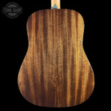 Close-up of the back of an acoustic guitar showing a rich, figured wood grain finish in warm brown tones, set against a solid black background with a Tone Shop logo in the top-left corner.