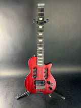 A red electric guitar with a cutaway body, mounted on a black stand against a dark gray studio background.