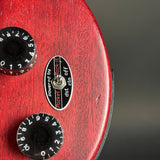 Close-up of a red guitar control panel with two black rotary knobs and a central black oval switch badge reading 'powered by Rocket by Jackson'.