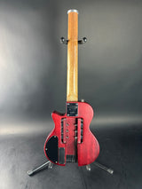 A red electric double-cutaway guitar with a natural wood neck, displayed upright on a black stand against a dark gray studio background.