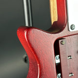 Close-up of a glossy red electric guitar body showing the wood grain finish, control plate, and silver hardware against a dark gray background.