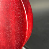 Close-up of a glossy red guitar body edge with visible wood grain and small surface scratches, photographed against a dark gray background.