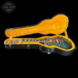 A closed black hard guitar case with a bright yellow-orange velvet interior, shown open against a black background. A blue-green electric guitar rests inside the case.