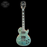 A Gibson electric guitar with a distinctive turquoise and teal flame maple top, shown against a solid black background. A Tone Shop watermark is visible in the upper left corner.