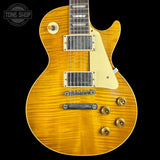 A close-up of a Gibson Les Paul Custom electric guitar with a vibrant flamed maple top in a golden yellow finish, featuring a cream pickguard and gold hardware, set against a solid black background.