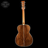 Back view of a wooden acoustic guitar on a black background with 'Tone Shop' logo.