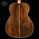 Back view of a wooden acoustic guitar with 'Tone Shop' logo.