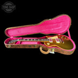 A gold electric guitar inside an open pink-lined hard case with a brown wood-grain exterior, shown against a black background. A Tone Shop watermark is visible in the top-left corner.