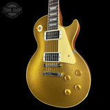 A gold glitter electric guitar with a cream pickguard and chrome hardware, shown against a solid black background with a Tone Shop watermark in the top-left corner.