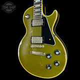 A used Gibson Les Paul Custom electric guitar with a distressed olive green finish, black pickguard, and gold-toned hardware, shown against a black background with a Tone Shop watermark in the top left corner.