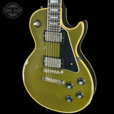 A classic Gibson Les Paul Custom electric guitar with a distressed olive green finish, black pickguard, and gold-toned hardware, shown against a solid black background.