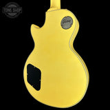 The back of a yellow Gibson electric guitar, showing the body, pickguard, and Gibson logo badge against a black background.