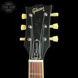 Close-up of a Gibson Les Paul Deluxe acoustic guitar headstock against a black background, showing the Gibson logo, Les Paul Model text, a Tune Shop watermark, and cream-colored tuning pegs.