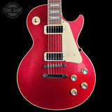 A red glitter electric guitar with a cream pickguard, gold hardware, and a black bridge, shown against a solid black background. A Tone Shop watermark is visible in the top left corner.
