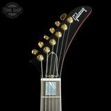 Close-up of the headstock of a Gibson electric guitar against a solid black background, showing gold tuning pegs, white Gibson branding, and part of the fretboard.