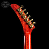 Close-up of the headstock of a Gibson electric guitar with a glossy red cherry finish and gold tuning pegs, set against a solid black background.