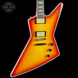 A Fender electric guitar with a vibrant sunburst finish, transitioning from bright orange to deep red. It features a distinctive angular body shape, dual humbucker pickups, and black control knobs, shown against a solid black background with a Tone Shop watermark in the top left corner.