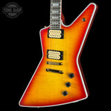 A classic electric guitar with a distinctive angular body, featuring a vibrant sunburst finish that transitions from a bright yellow-orange center to deep red and black edges. It is shown against a solid black background with a Tone Shop watermark in the upper left corner.