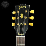 Close-up of a Gibson electric guitar headstock with a black finish, gold logo and tuning pegs, shown against a black background.