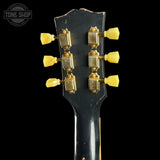 Close-up of the headstock of a black electric guitar, showing six gold tuning pegs with translucent yellow caps against a black background.