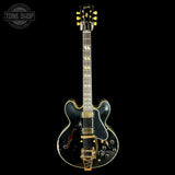 A black electric guitar with gold hardware and gold-toned tuning pegs, shown from the front against a solid black background. A circular 'TONE SHOP' watermark is visible in the top-left corner.