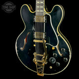 A black Gibson electric guitar with gold hardware and trim, shown against a solid black background. The Gibson logo is visible on the headstock (partially cropped) and on the gold tremolo tailpiece.