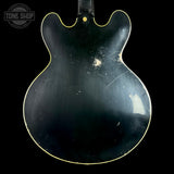 The back of a black electric guitar body with a gold binding edge, showing significant wear, scratches, and scuffs on the glossy finish, set against a solid black background with a Tone Shop watermark in the top-left corner.