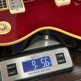A close-up of a red electric guitar resting on a digital scale displaying 9.56 lbs.