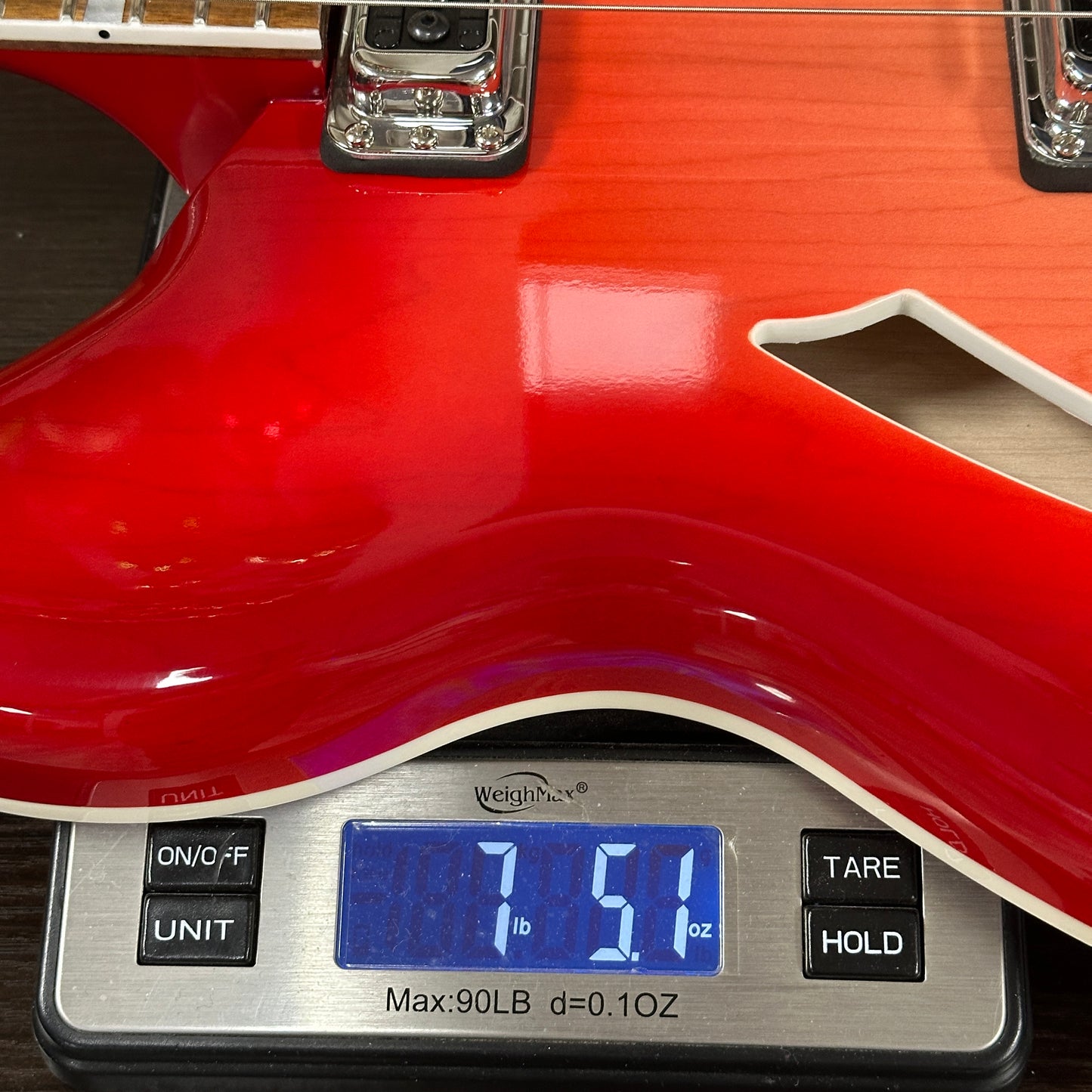 Red electric guitar on a digital scale displaying weight.