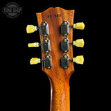 Close-up of the headstock of an electric guitar, showing six black tuning machines with yellow tuning keys and the serial number 951283 printed on the back, set against a solid black background.