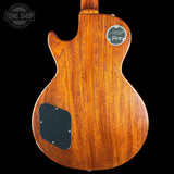 The back of a Gibson Les Paul Custom electric guitar, featuring a rich reddish-brown wood grain finish, a black pickguard, and a Gibson logo badge on a solid black background.