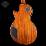 The back of a Gibson electric guitar made of rich, warm brown wood, featuring a black pickguard and a silver metal output jack, shown against a solid black background.