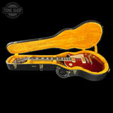 A red electric guitar inside an open black hard case with a bright yellow-orange velvet interior, shown against a black background. A Tone Shop watermark is visible in the top-left corner.