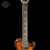 Close-up of an electric guitar neck and lower body against a black background, featuring a sunburst wood finish, bird inlays on the fretboard, and a Tone Shop watermark in the upper left.
