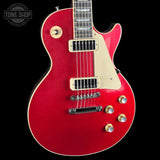 A red electric guitar with a cream pickguard and gold-toned hardware, shown against a solid black background. A Tone Shop watermark is visible in the top-left corner.