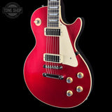 A red electric guitar with a cream pickguard and gold-toned hardware, shown against a solid black background. A Tone Shop watermark is visible in the top-left corner.