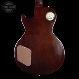 The back of a Gibson electric guitar with a glossy dark brown cherry finish, featuring a circular Gibson logo badge and a maple pickguard, shown against a solid black background.