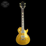A gold-finish electric guitar, identified as a Gibson Les Paul Custom, shown against a solid black background with a Tone Shop watermark in the top-left corner.