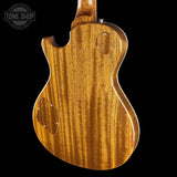 Close-up of the back of an electric guitar body made of figured wood with a glossy warm honey finish, shown against a black background with a Tone Shop watermark in the top left.