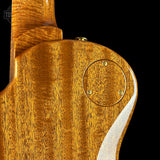 Close-up detail of an electric guitar's back end, showcasing a rich, glossy natural wood finish with prominent grain patterns and a circular soundhole surround on a solid black background.