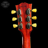 Close-up of the headstock of a guitar against a black background, showing six black tuning pegs with yellow knobs and the serial number 961198 printed on the glossy red wood back.