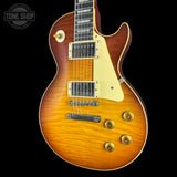 A classic electric guitar with a sunburst finish, featuring a warm orange and yellow burst pattern, a cream pickguard, and gold hardware, shown against a solid black background with a Tone Shop watermark in the top left corner.
